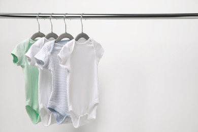 Baby bodysuits hanging on rack near white wall. Space for text