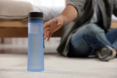 Photo of Man taking transparent plastic bottle with water while sitting on floor at home, closeup