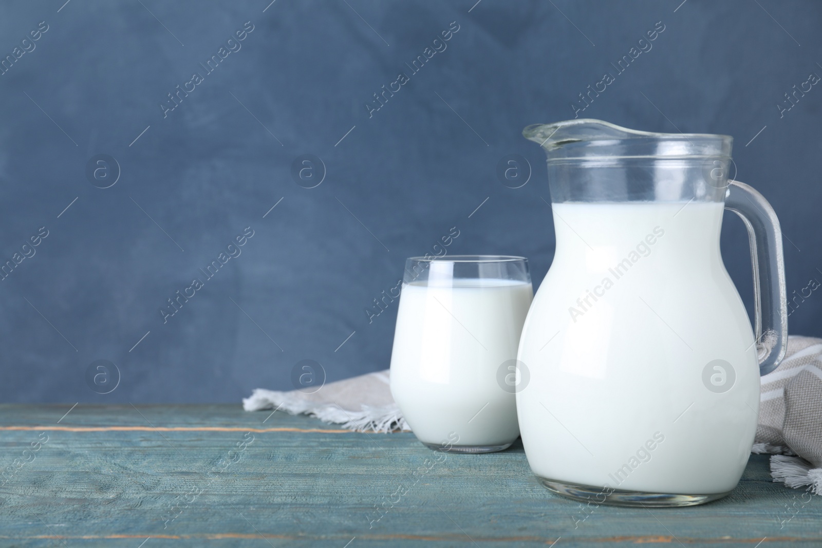 Photo of Jug and glass with fresh milk on wooden table against blue background. Space for text