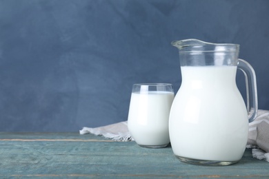 Photo of Jug and glass with fresh milk on wooden table against blue background. Space for text