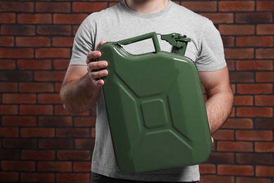 Photo of Man holding khaki metal canister against brick wall, closeup