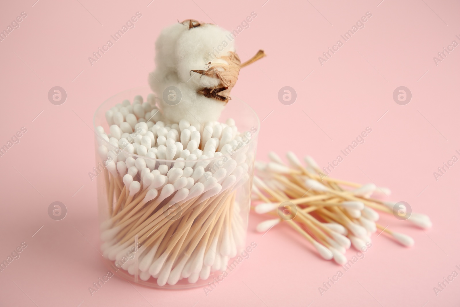 Photo of Container with cotton buds and flower on pink background