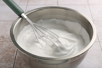 Bowl and whisk with whipped cream on tiled table