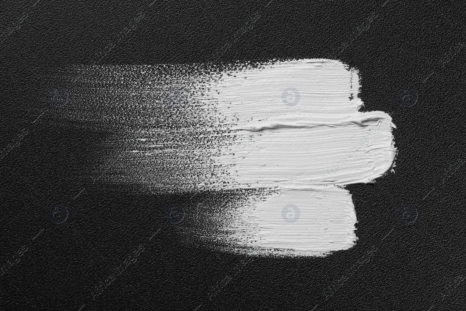 Photo of Strokes of white oil paint on black canvas, top view