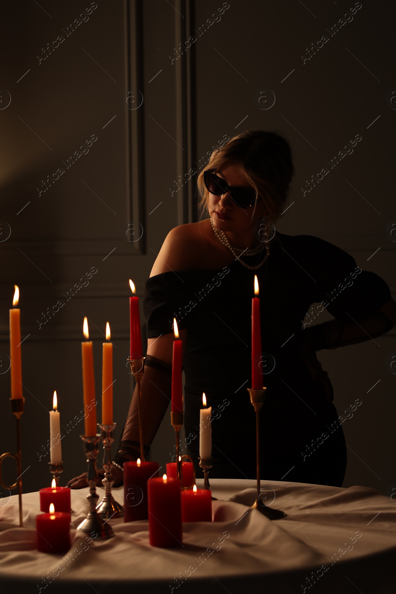 Photo of Beautiful young woman in sunglasses near table with burning candles at night