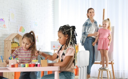 Female teacher with child near easel at painting lesson indoors