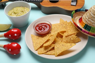 Nachos chips, sauce, Mexican sombrero hat, maracas and guacamole on light blue background
