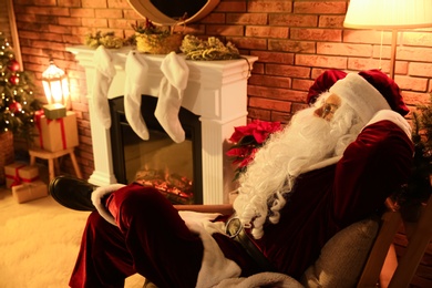 Santa Claus resting near decorated fireplace indoors