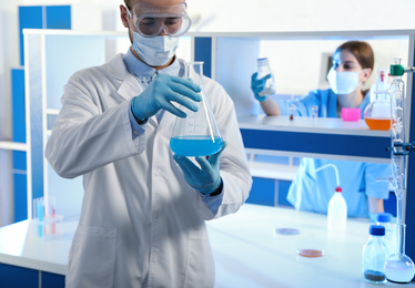 Photo of Scientist holding conical flask with blue liquid indoors. Laboratory analysis