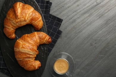 Delicious fresh croissants and cup of coffee on gray table, flat lay. Space for text