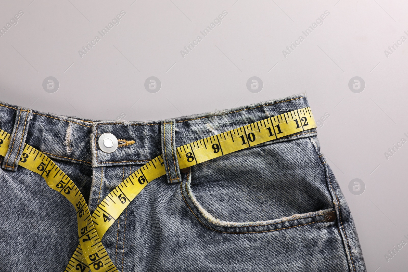 Photo of Jeans with measuring tape on light grey background, top view and space for text. Weight loss concept
