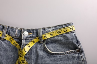 Photo of Jeans with measuring tape on light grey background, top view and space for text. Weight loss concept