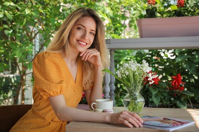 Photo of Happy young woman with cup of coffee and magazine enjoying early morning in outdoor cafe