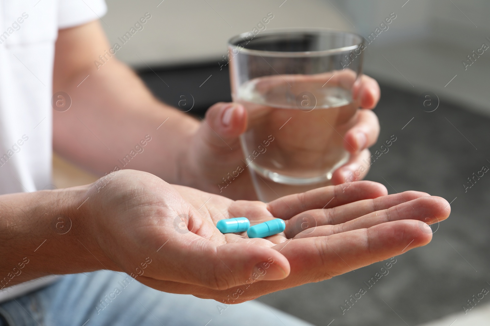 Photo of Man with glass of water and pills on blurred background, closeup