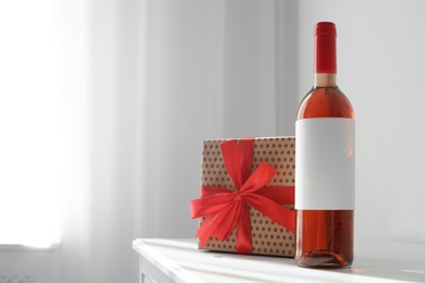 Photo of Bottle of wine and gift box on table in light room. Space for text