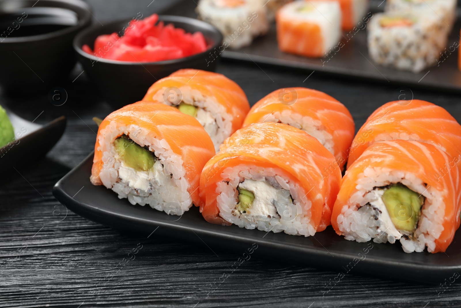 Photo of Tasty sushi rolls with salmon on black wooden table, closeup