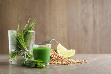 Photo of Composition with glass of wheat grass juice and grains on table. Space for text
