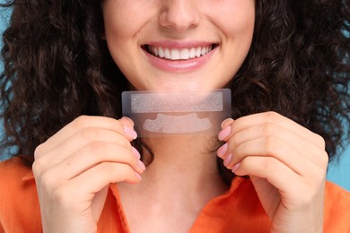 Photo of Young woman holding teeth whitening strips on light blue background, closeup