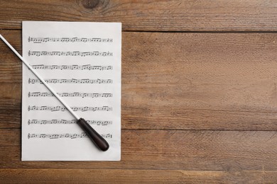 Conductor's baton and sheet music on wooden table, top view. Space for text