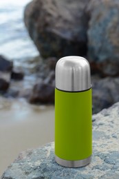 Metallic thermos with hot drink on stone near sea, space for text