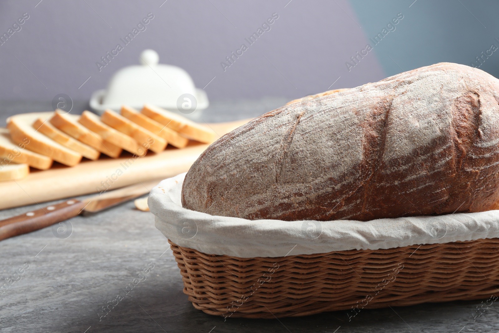 Photo of Loaf of tasty fresh bread in wicker basket on grey table, closeup