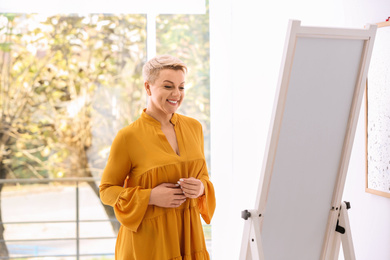 Beautiful mature woman looking at herself in large mirror indoors