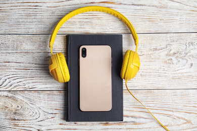 Book, modern headphones and smartphone on white wooden table, flat lay