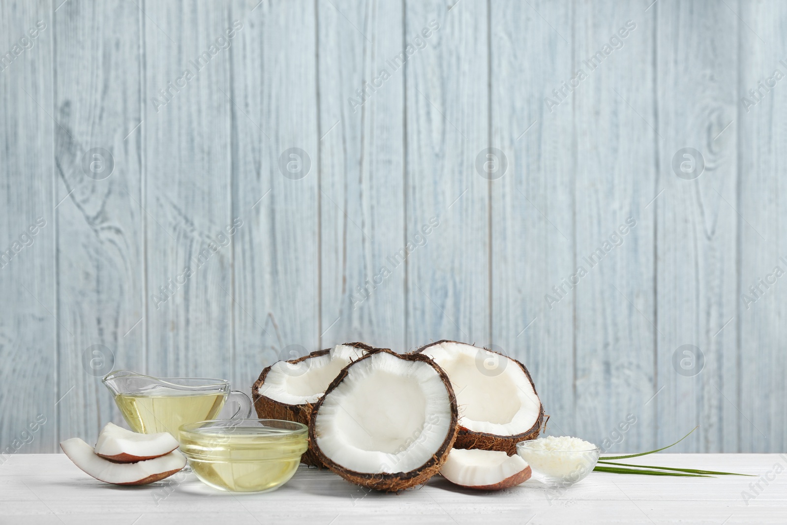 Photo of Glassware with natural organic oil and coconuts on white wooden table. Space for text