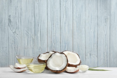 Glassware with natural organic oil and coconuts on white wooden table. Space for text