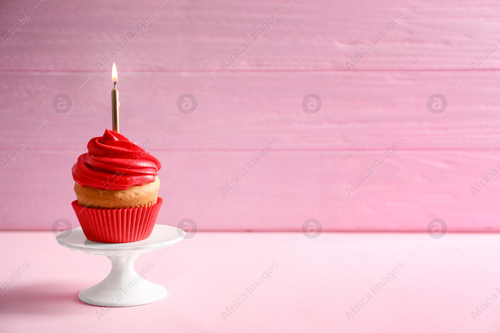 Photo of Delicious birthday cupcake with burning candle on table against color background