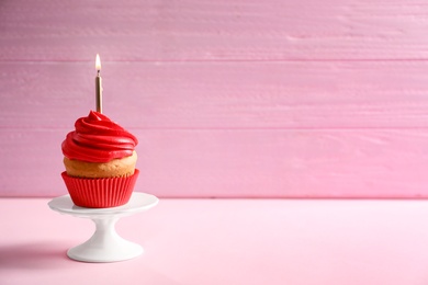 Photo of Delicious birthday cupcake with burning candle on table against color background