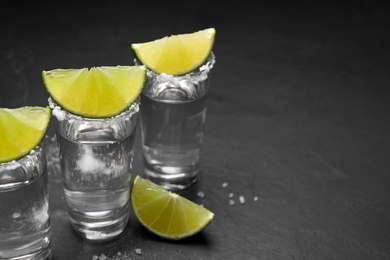 Photo of Mexican Tequila shots, lime slices and salt on black table. Space for text