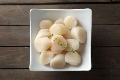 Photo of Fresh raw scallops and thyme in bowl on wooden table, top view