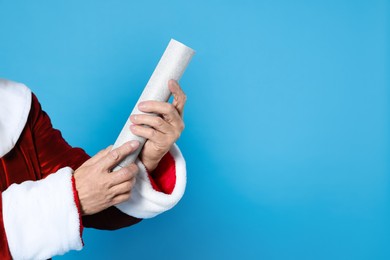Photo of Man in Santa Claus costume with party popper on light blue background, closeup. Space for text