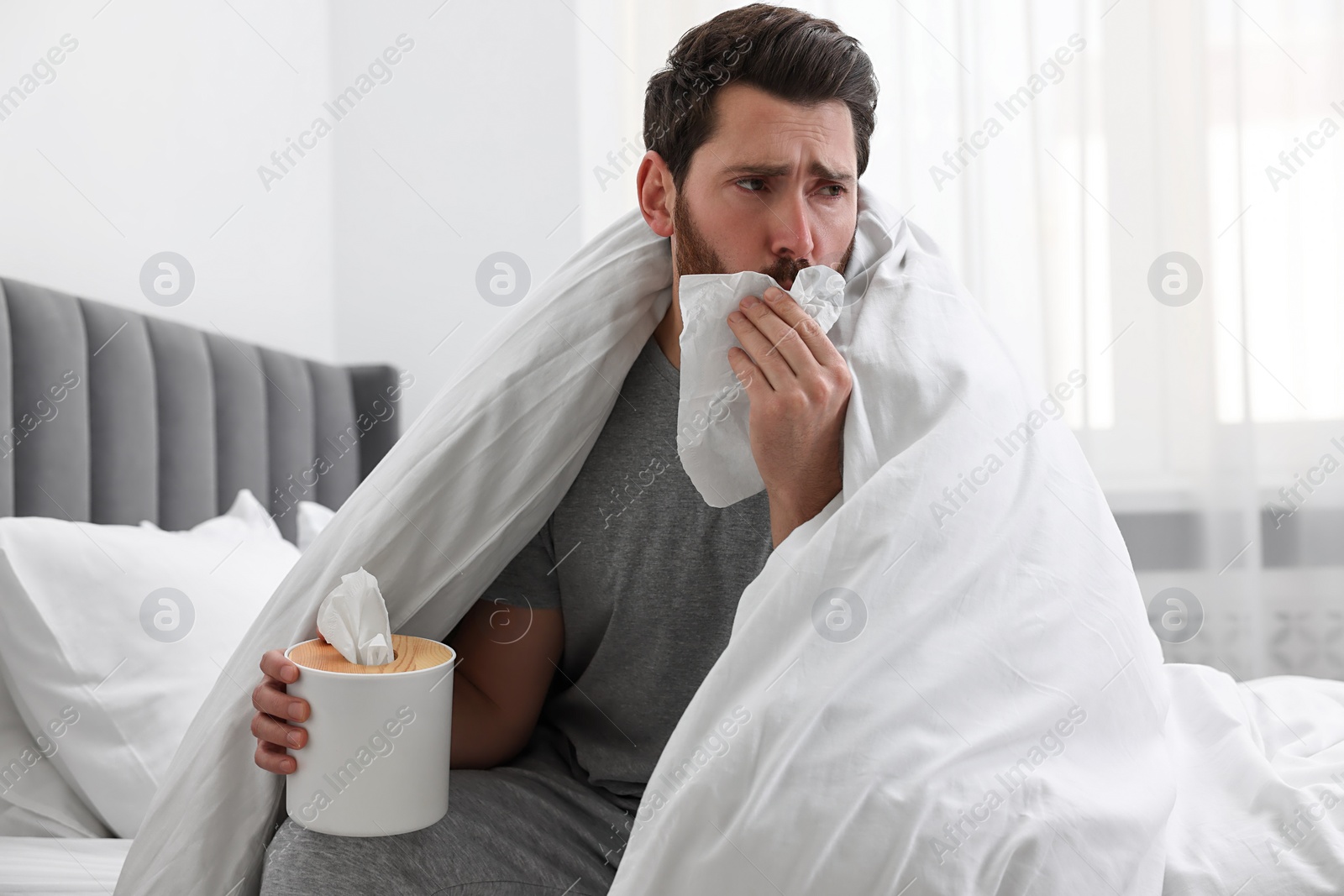 Photo of Sick man with tissue coughing on bed at home. Cold symptoms