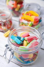 Tasty jelly candies in different jars on white wooden table