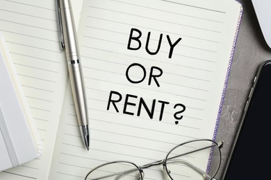 Image of Buy or rent - choice concept. Notebook, pen, glasses and smartphone on grey table, flat lay