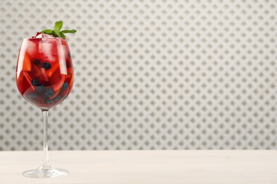Photo of Glass of Red Sangria with fruits on white wooden table, space for text