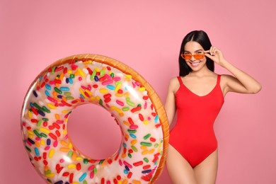 Photo of Young woman with stylish sunglasses holding inflatable ring against pink background
