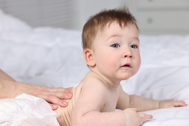 Photo of Woman applying body cream onto baby`s back on bed, closeup