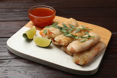 Photo of Tasty fried spring rolls, lime, arugula and sauce on wooden table, closeup