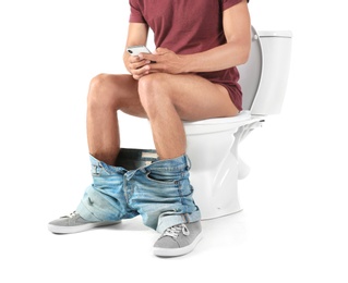 Photo of Young man using mobile phone while sitting on toilet bowl. Isolated on white