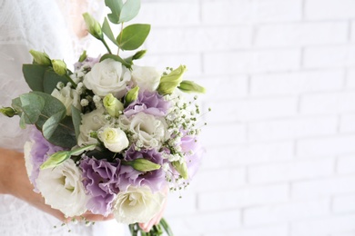 Photo of Bride holding beautiful bouquet with Eustoma flowers near brick wall, closeup. Space for text