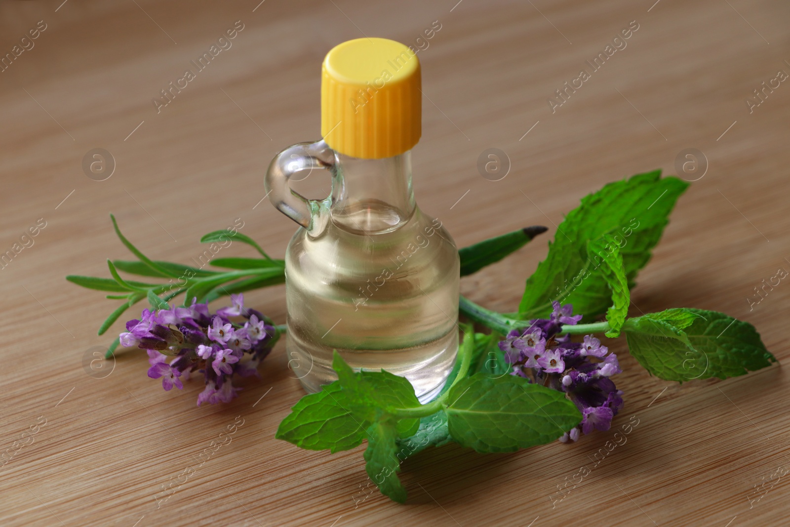 Photo of Bottle of natural essential oil, mint leaves and lavender flowers on wooden table, closeup