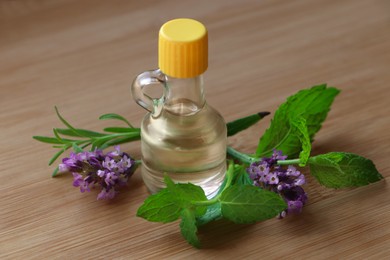 Bottle of natural essential oil, mint leaves and lavender flowers on wooden table, closeup