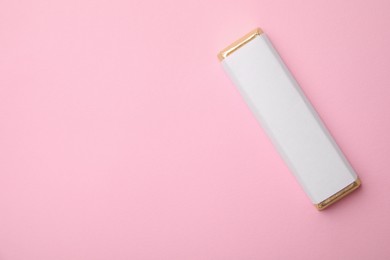 Tasty chocolate bar in package on pink background, top view. Space for text
