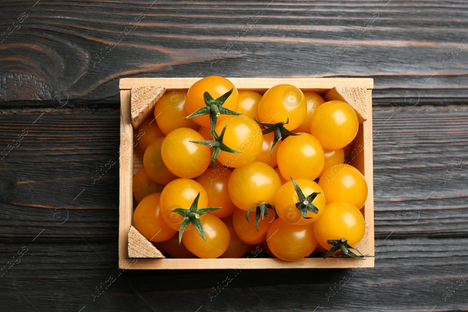 Photo of Ripe yellow tomatoes in crate on dark wooden table, top view