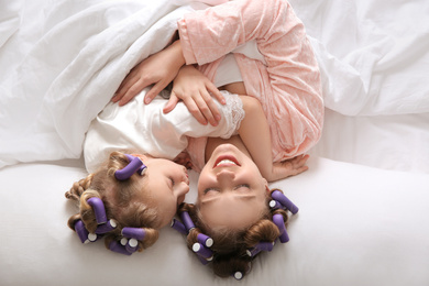Photo of Happy mother and daughter with curlers lying on bed, above view