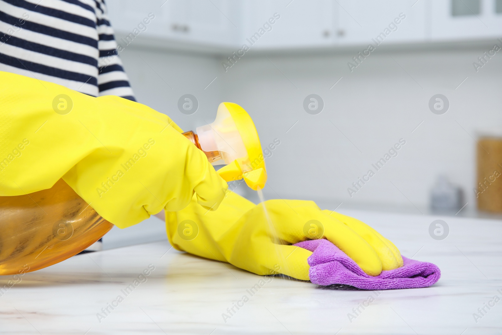 Photo of Woman cleaning white surface with detergent and purple rag indoors, closeup