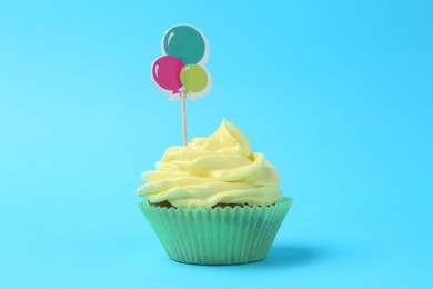 Photo of Delicious cupcake with bright cream and topper on light blue background